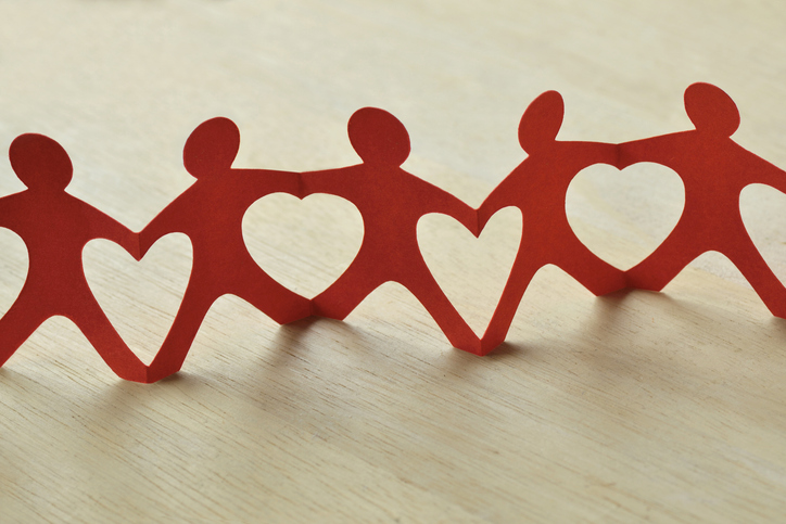 A red paper chain of people on a table, their arms and legs connecting, making heart-shaped cutouts. Choosing charitable organizations.